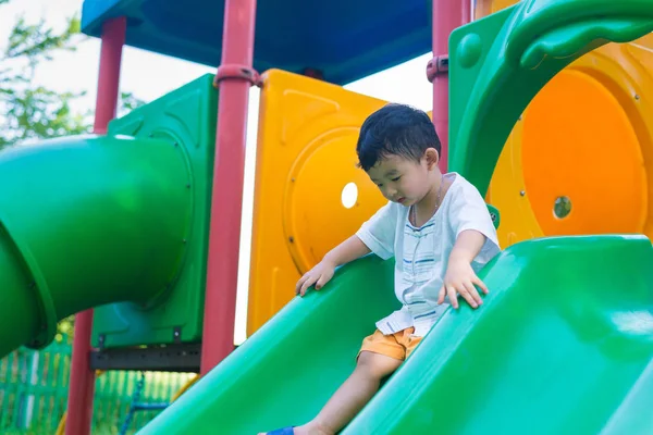 Pequeño niño asiático jugando diapositiva en el patio de recreo bajo el sunli — Foto de Stock