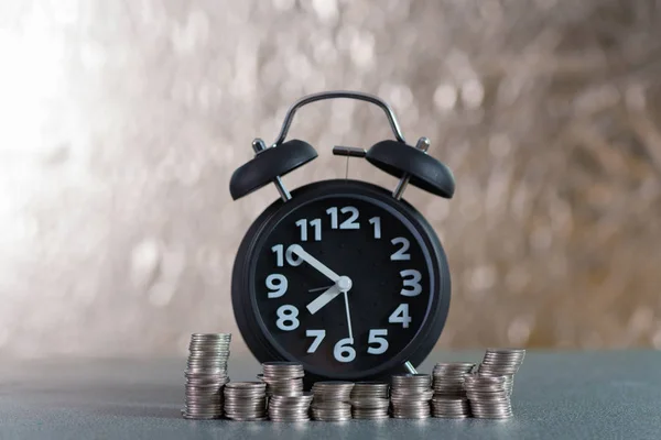 Relógio de alarme e passo de pilhas de moedas na mesa de trabalho, tempo para — Fotografia de Stock