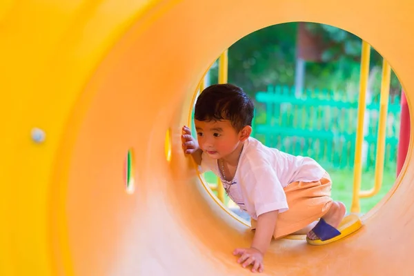 Bonito ásia menino jogar e sorrindo no amarelo túnel no o playg — Fotografia de Stock