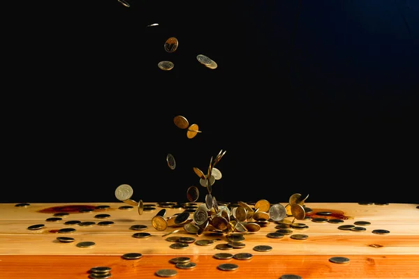 Falling gold coins money on wooden table with black wall, copy s