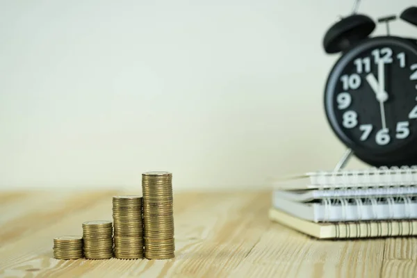 Pasos de pila de monedas con reloj despertador vintage y pluma, portátil — Foto de Stock