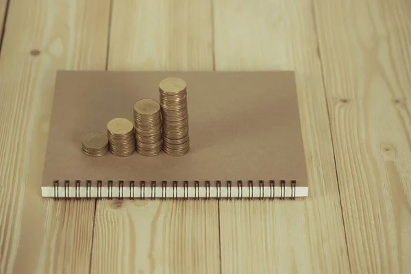 Pasos de pila de monedas con papel de cuaderno en la mesa de trabajo de madera — Foto de Stock