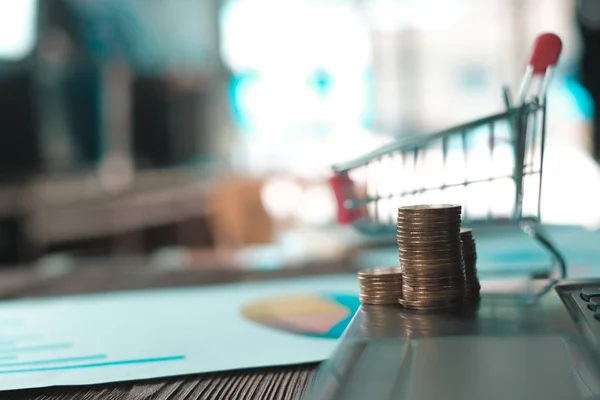 Step of coins stacks with trolley and notebook laptop computer and financial graph on white paper on working table, business planning vision and finance analysis concept idea. and copy space for add text.