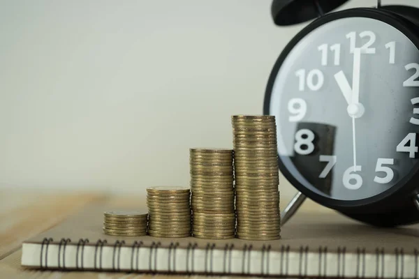 Pasos de pila de monedas con reloj despertador vintage y pluma, portátil —  Fotos de Stock