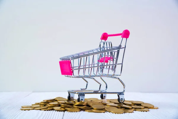 Piles of coins and shopping cart or supermarket trolley on white — Stock Photo, Image