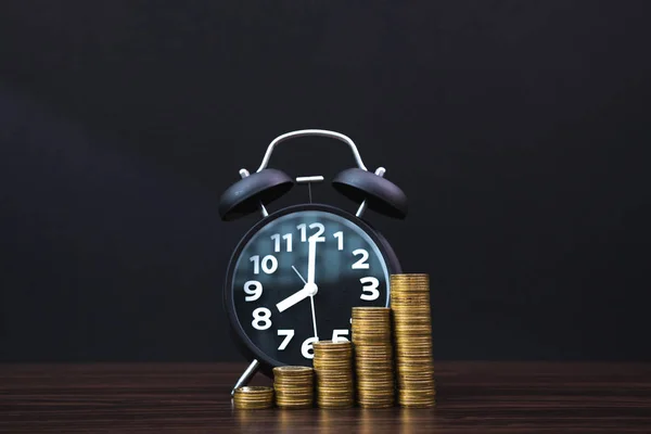 Relógio de alarme e passo de pilhas de moedas na mesa de trabalho no escuro ro — Fotografia de Stock