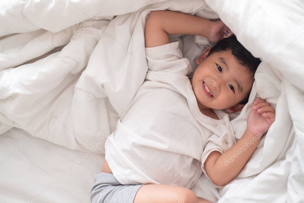 3 years old little cute Asian boy at home on the bed, kid lying 