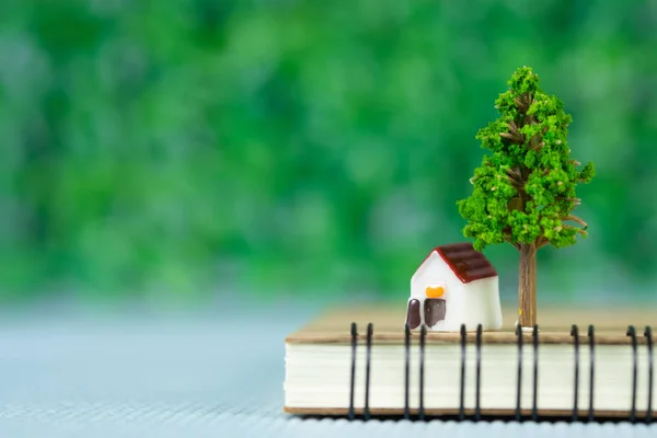 Pequena casa modelo e pequena árvore com notebook, poupança bancária — Fotografia de Stock