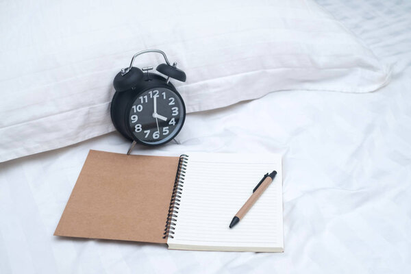 Diary or notebook and vintage alarm clock on bed in bedroom at h