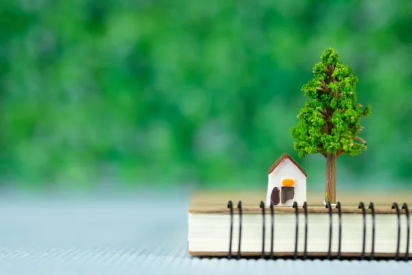 Pequena casa modelo e pequena árvore com notebook, poupança bancária — Fotografia de Stock