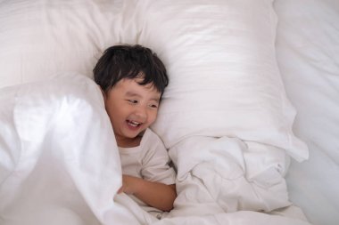 3 yıl eski küçük şirin Asyalı çocuk beyaz gömlek evde yatakta, çocuk oyun yalan ve beyaz yatak yastık ve battaniye ile gülümseyen, kopya alanı olan Üstten Görünüm Ekle metin.