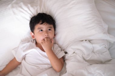 3 yıl eski küçük şirin Asyalı çocuk beyaz gömlek evde yatakta, çocuk oyun yalan ve beyaz yatak yastık ve battaniye ile gülümseyen, kopya alanı olan Üstten Görünüm Ekle metin.