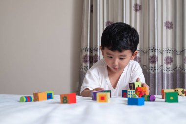 3 yıl eski küçük şirin Asyalı çocuk oynamak oyuncak ya da kare blok bulmaca evde yatakta, yalan blok şekli veya parçalar, eğitim ve sağlıklı kavramı oynayarak öğrenmek.