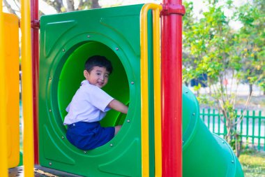 Asyalı çocuk bahçesi içinde güneş ışığı altında slayt oynayan 