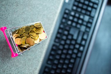 Online alışveriş, e-ticaret ve iş konsepti için bilgisayar ve klavyeli süpermarket arabasında madeni paralar