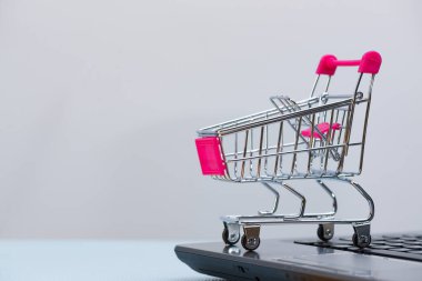 Gri arka plan ve fotokopi alanı, e-ticaret ve çevrimiçi alışveriş konsepti üzerine dizüstü bilgisayarı olan alışveriş arabası veya süpermarket tramvayı.