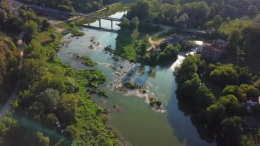 Nehir köprüsünün üzerinde uçmak, nehrin üzerinde güzel bir hava manzarası, küçük bir şehirdeki akşam nehrinin havadan manzarası.