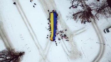 Kışın Ukrayna bayrağının havadan görünüşü, çocukların üstten görünüşü Ukrayna 'nın büyük bir bayrağını taşıyor, kış karında oynayan insanların en üst görüntüsü, neşeli çocuklar üzerinde uçan insansız hava aracı.
