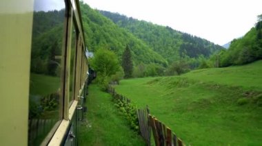 Eski bir tren vagonunun penceresinden manzara, Romanya 'da eski bir buhar lokomotifi, buharlı dar ölçü treni, kırsal alanda tıkırdayan buhar treni, dar ölçülü demiryolu.