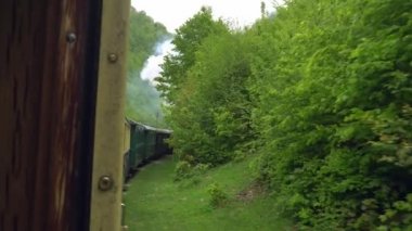 Eski bir tren vagonunun penceresinden manzara, Romanya 'da eski bir buhar lokomotifi, buharlı dar ölçü treni, kırsal alanda tıkırdayan buhar treni, dar ölçülü demiryolu.