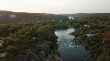 Nehrin güneş doğarken hızlı akışını, nehirdeki kayaların üzerinden uçuşu, nehirli granit kayalar, gündoğumunda nehrin havadan görünüşü ve yeşil ağaçlar