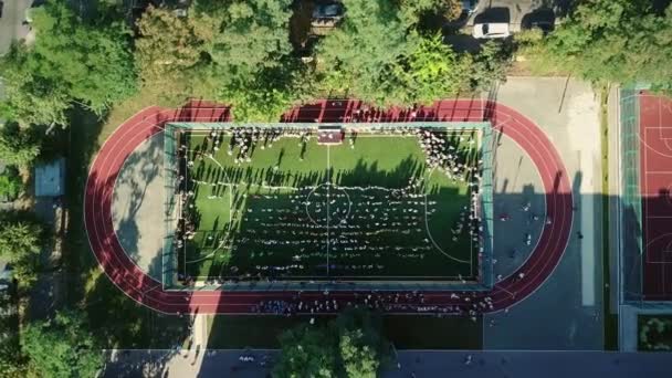 学校のスタジアムで踊る子供たちの空中ビュー 市内の学校のスタジアムでの子供たちの空中ビュー 遊び心のある子供たちに対する頭上の空中ドローン飛行 屋外サッカー場の空中映像フィールド — ストック動画