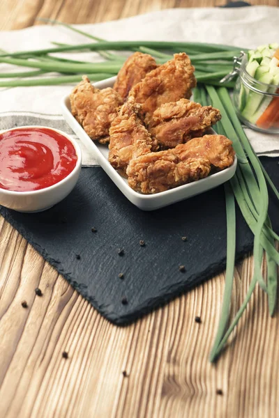 Parts of chicken wings in breading with tomato sauce on brown wooden table