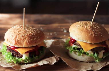 Sığır eti, salata ve ahşap masa üzerinde peynir ile iki el yapımı hamburger.