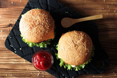 Sığır eti, salata ve ahşap masa üzerinde peynir ile iki el yapımı hamburger.