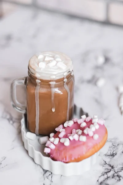 Rosado donut con malvavisco y chocolate caliente en taza de vidrio sobre mesa de mármol . — Foto de Stock