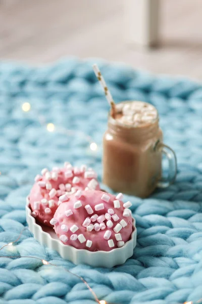 Donut rosa con malvavisco y chocolate caliente en taza de vidrio sobre manta de punto merino azul. Luces sobre fondo — Foto de Stock