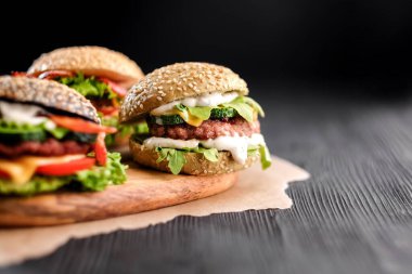 Biftek, salata, peynir, domates, susam tohumu, siyah ahşap masada domuz pastırması.