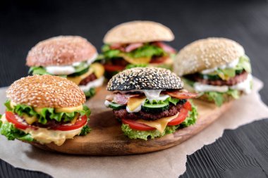 Biftek, salata, peynir, domates, susam tohumu, siyah ahşap masada domuz pastırması.