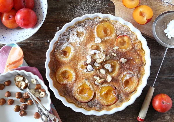 Autumn dessert. Red plums clafoutis, hazelnut and icing sugar dr — Stock Photo, Image