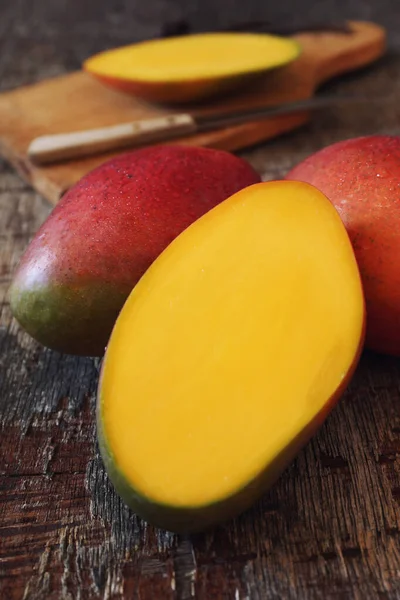 Frutas tropicais de manga, intactas e meia em tábua de corte de madeira — Fotografia de Stock