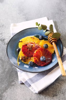 Citrus tatlısı. Bal, baharat ve yaban mersinli turuncu carpaccio sarı ve kan portakallı koyu arkaplanda.
