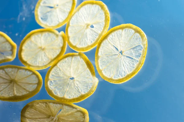 Hanging, falling and flying slice of lemon on blue background — Stock Photo, Image