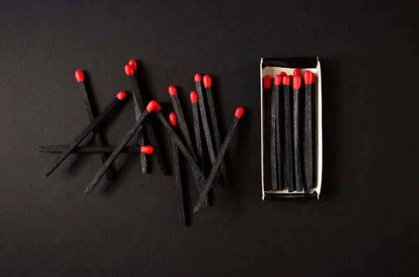 Black wood matches with red heads on dark black paper background. Creative flat lay, top view.