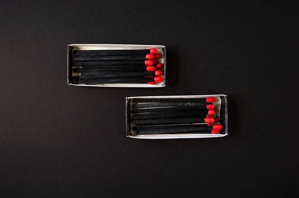 Black wood matches with red heads on dark black paper background. Creative flat lay, top view.