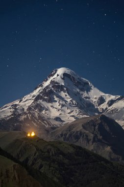 Mount Kazbek karlı zirvesine Georgia Gergeti Trinity Kilisesi ile yıldızlarla dolu bir gökyüzü altında geceleri.