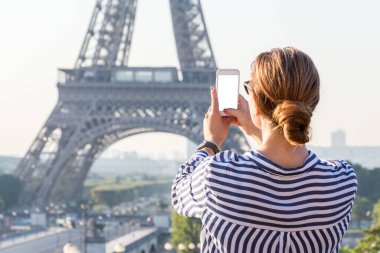 Güzel kız Paris, Fransa 'daki ünlü Eyfel Kulesi' nin akıllı telefonuyla fotoğraf çekiyor. Telefon ekranı beyaz model.