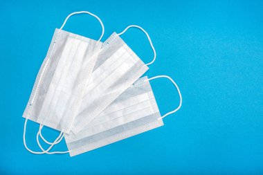 Plastik kulaklıklı üç cerrahi maske. Ağız ve burnu örtmek için tipik 3 katlı cerrahi maske. Bakterilerin prosedür maskesi. Koruma konsepti. Mavi arkaplanda.