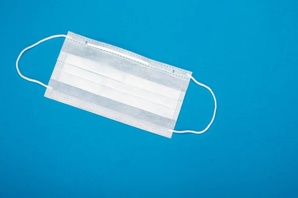 Surgical mask with rubber ear straps. Typical 3-ply surgical mask to cover the mouth and nose. Procedure mask from bacteria. Protection concept. On blue background.