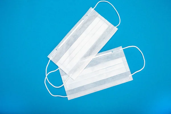 Two surgical masks with rubber ear straps. Typical 3-ply surgical mask to cover the mouth and nose. Procedure mask from bacteria. Protection concept. On blue background.