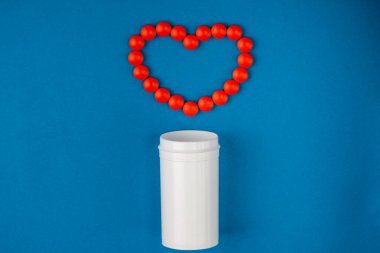 Kalp sağlığı konsepti. İlaç şişesi ve kırmızı ilaç hapları mavi arka planda kalp şeklinde..