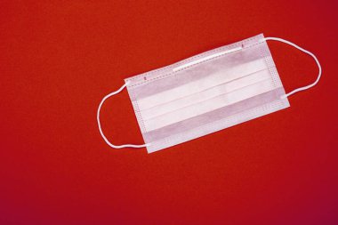 Plastik kulaklıklı cerrahi maske. Ağız ve burnu örtmek için tipik 3 katlı cerrahi maske. Bakterilerin prosedür maskesi. Koruma konsepti. Kırmızı arkaplanda.