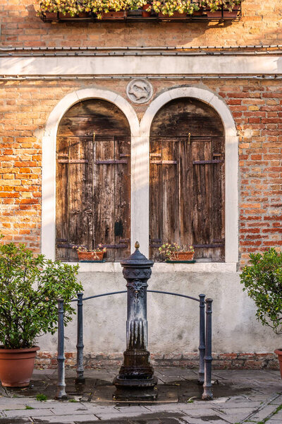 The fountain with drinking water. Picturesque brick house with windows and shutters Venice, Italy.