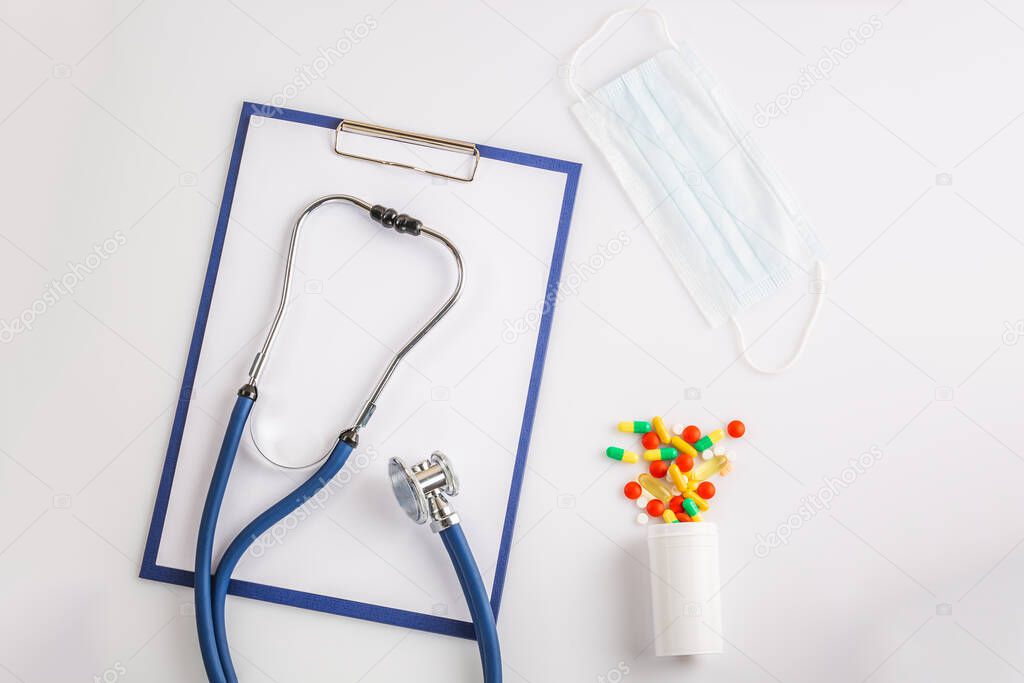 Stethoscope, clipboard, mask and colorful pills from the bottle on white background isolated on white. Concept of virus  2019-nCoV, coronavirus, illness. Medical check up.