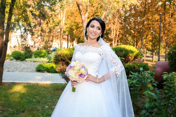 Bela noiva no dia do casamento no fundo da floresta de outono com um belo buquê — Fotografia de Stock