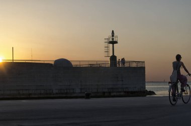 İnsanlar gün batımında limandaki silüeti